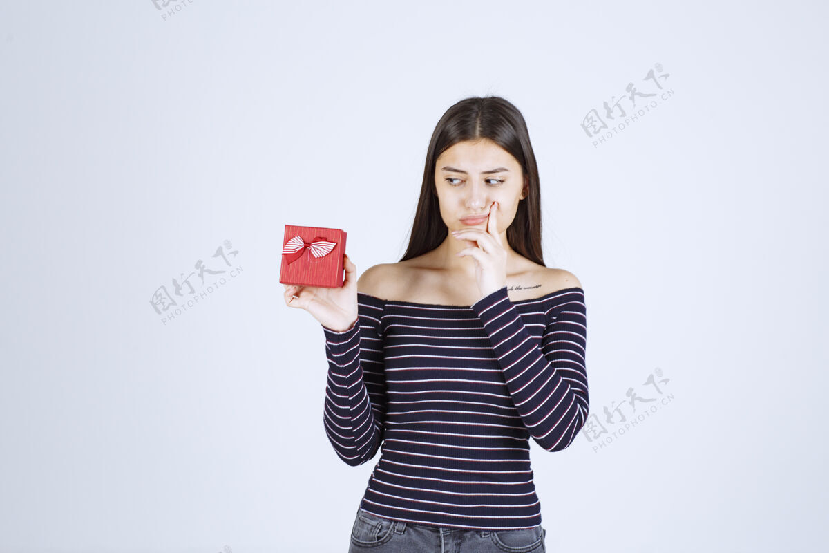 工人穿着条纹衬衫的女孩手里拿着一个红色的礼盒 看上去既困惑又怀疑恐惧奇怪激动