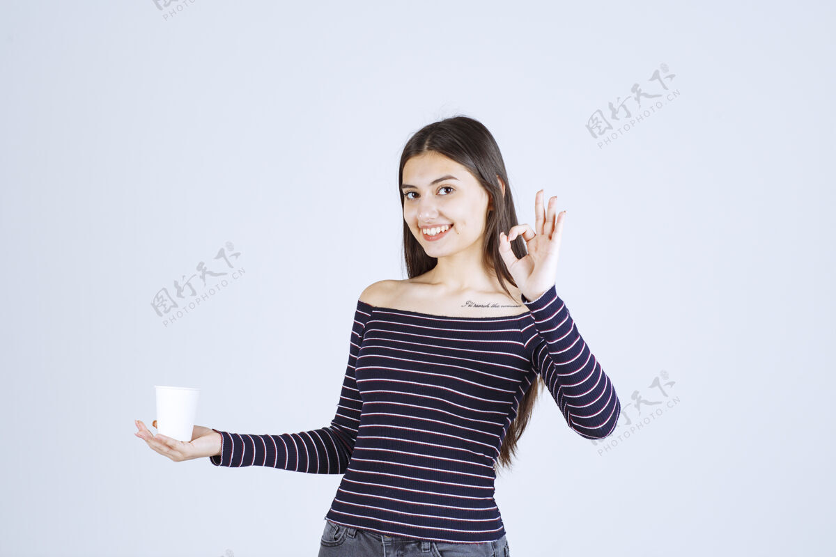 女人穿着条纹衬衫的女孩拿着一个塑料咖啡杯 指着一个好味道享受工人积极