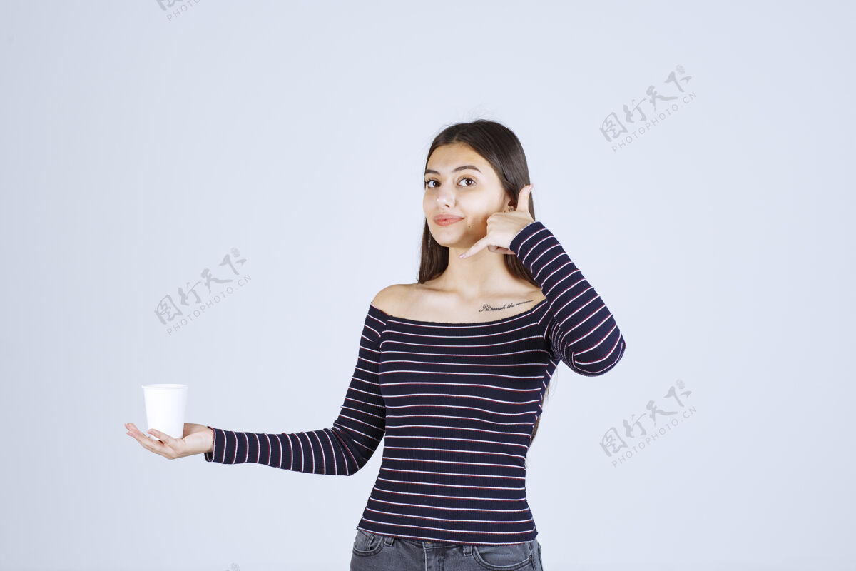 联系人穿着条纹衬衫的女孩拿着一个塑料咖啡杯 要打电话聪明女人年轻