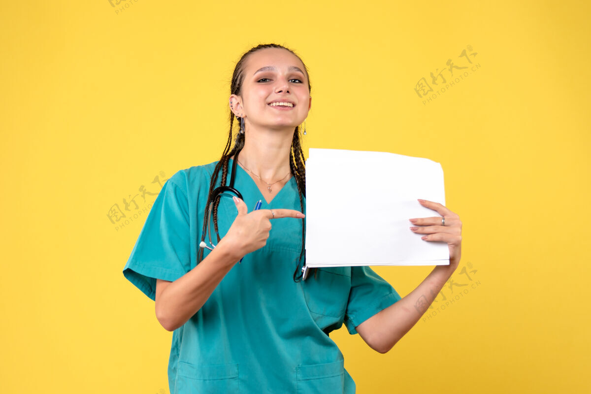 持有黄色墙壁上穿着医疗服拿着文件的女医生的正视图人医疗医生