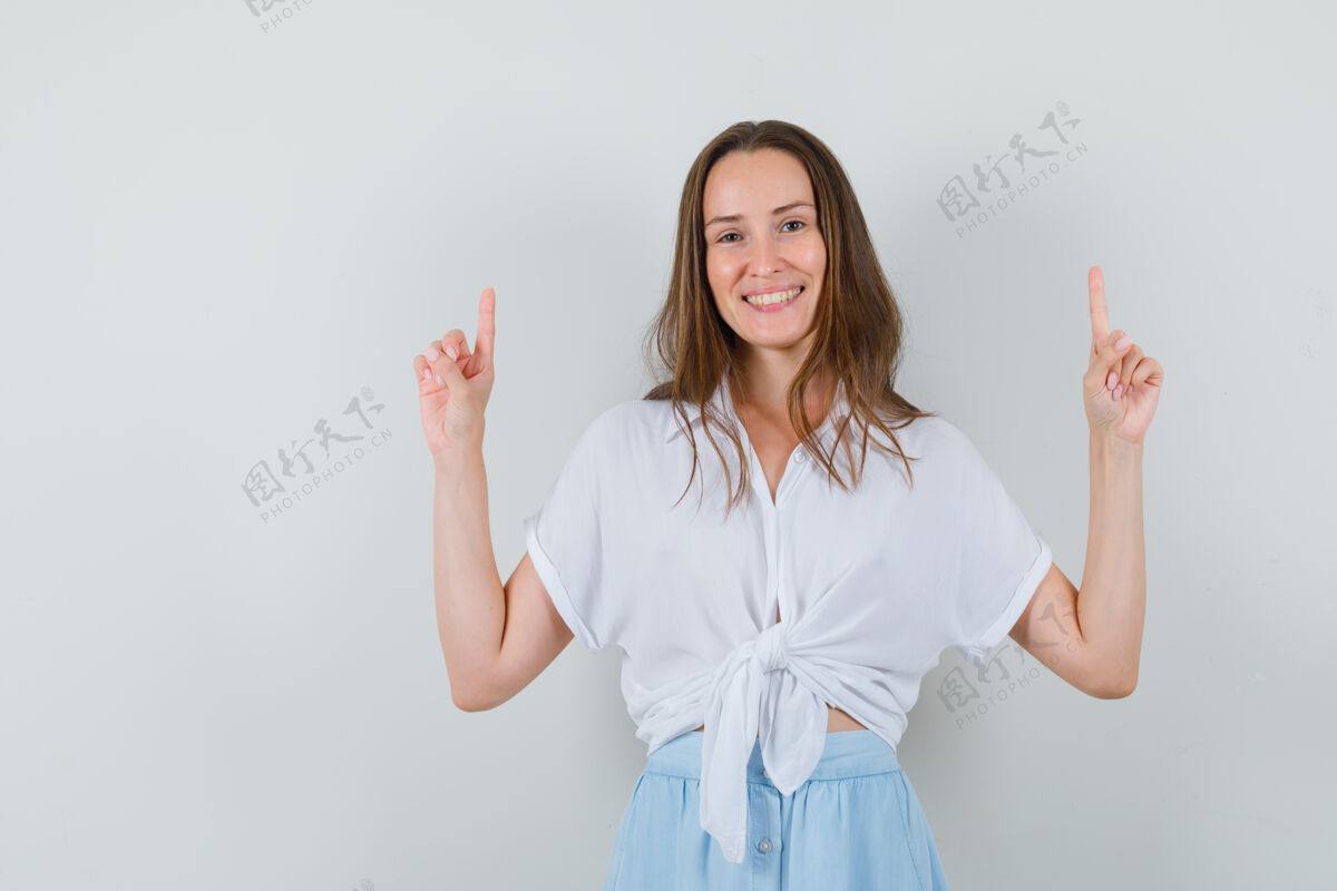 裙子穿着白衬衫和淡蓝色裙子的年轻女子用食指向上指着 看上去很高兴女人微笑头发