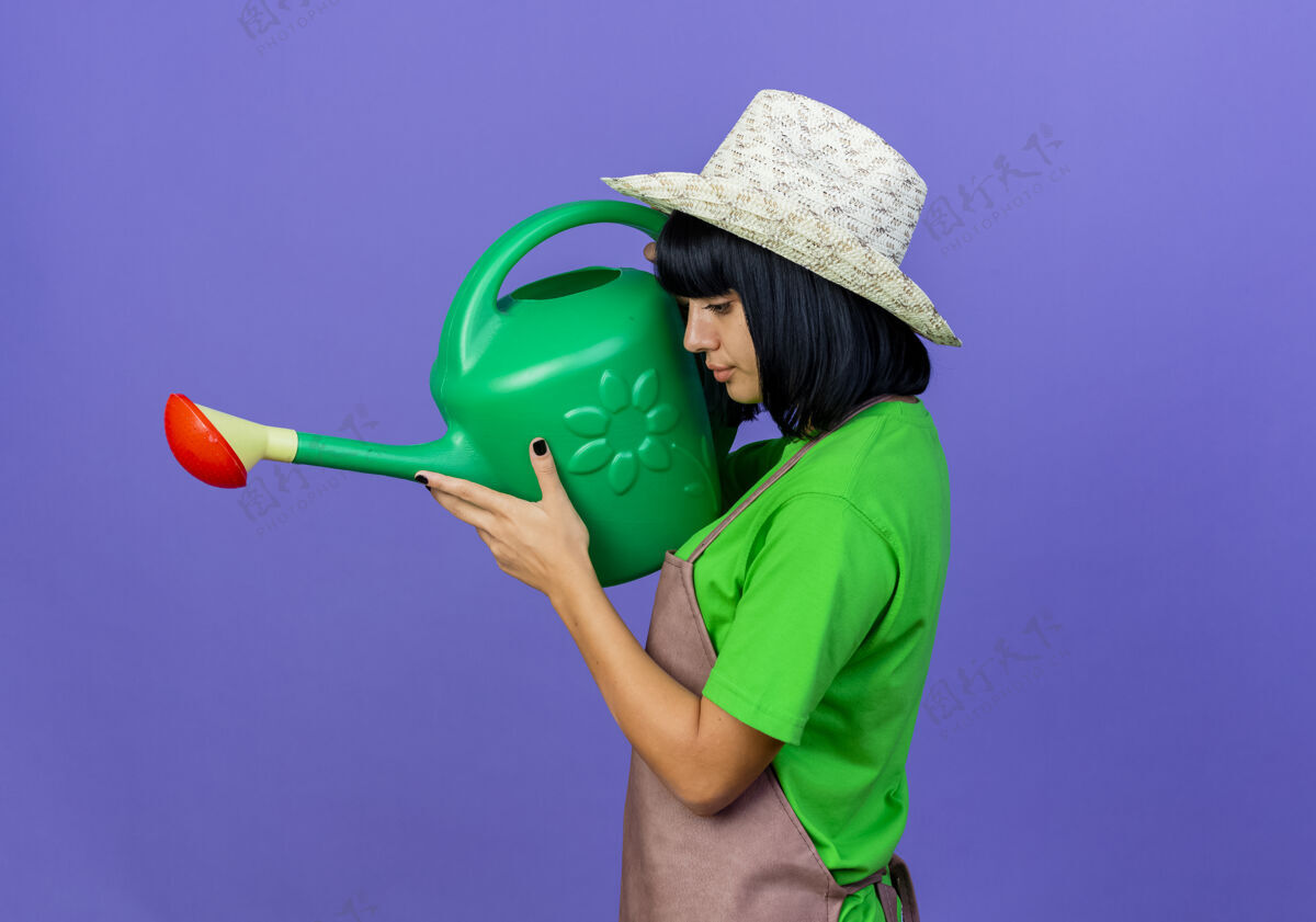 帽子自信的年轻女园丁穿着制服 戴着园艺帽 站在一边拿着浇水罐侧穿紫色