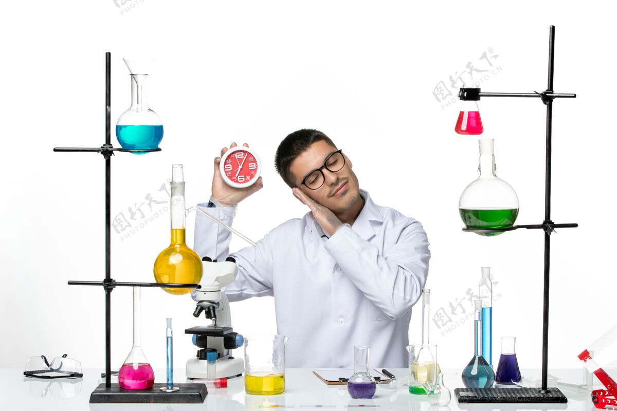医学正面图：身穿白色医疗服的男性化学家在浅白的办公桌上拿着时钟病毒疾病科学实验室covid视图罐子实验室