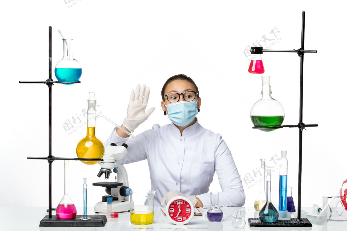 面具前视图穿着医疗服的女化学家戴着面罩坐着 拿着溶液 在浅白色背景上写笔记化学家实验室病毒covid-飞溅喷溅科学化学家