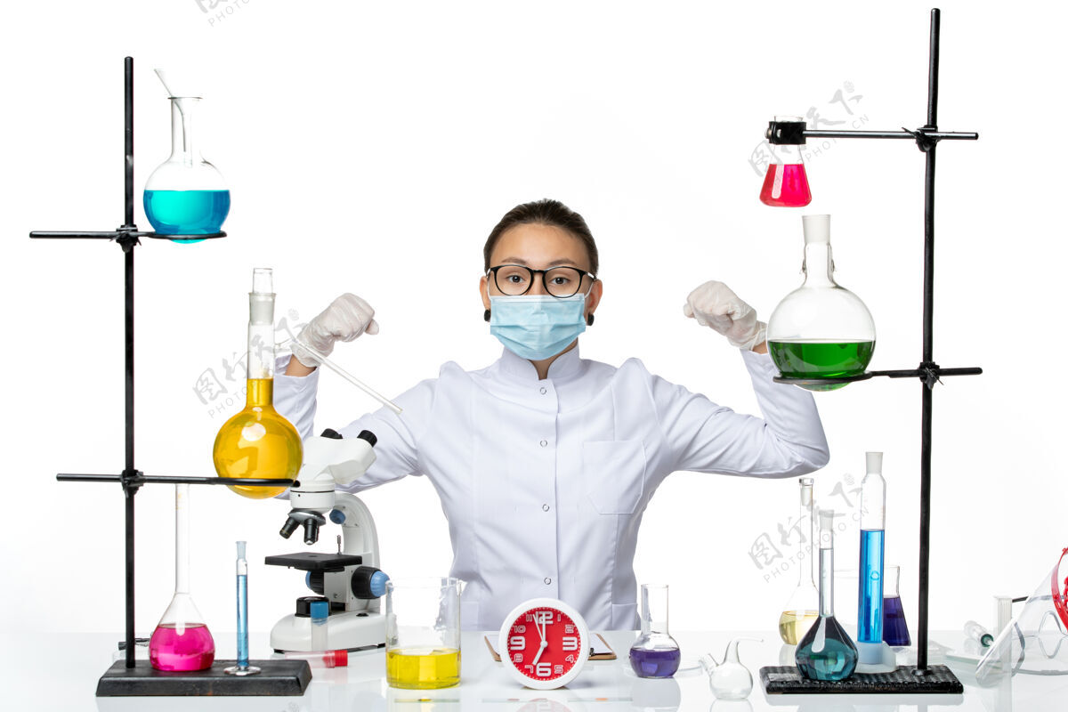 西装前视图：穿着医疗服的女化学家 戴着面罩 坐在溶液中 弯曲着白色背景病毒实验室化学冠状病毒飞溅物实验室面具医生