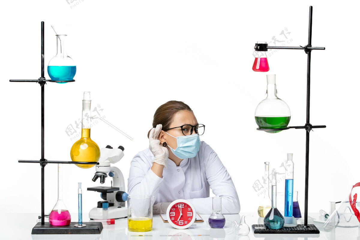 坐着前视图穿着医疗服的女化学家戴着面罩坐在溶液里 试图听到白色背景上飞溅的病毒化学covid实验室套装实验室烧杯