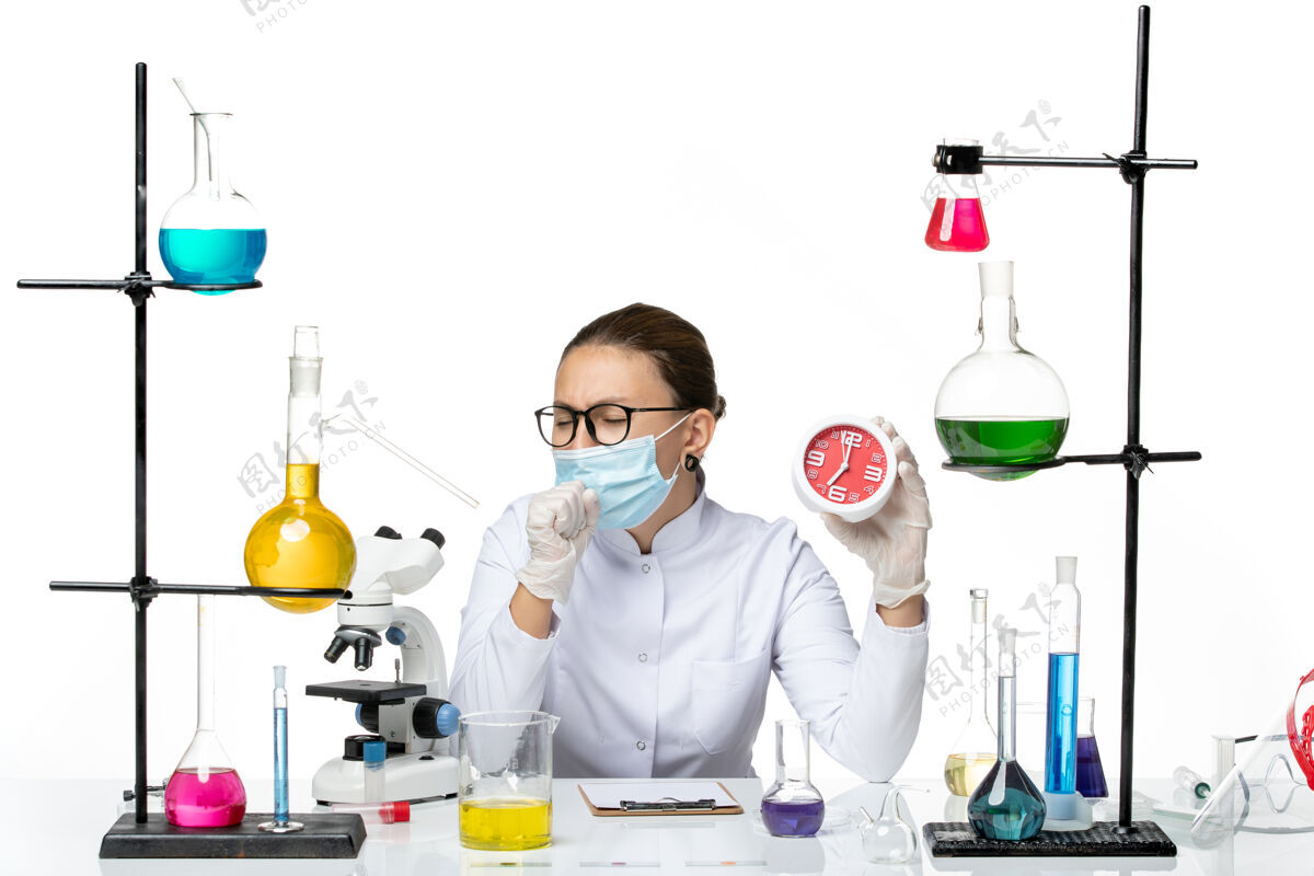 咳嗽前视图：身穿医疗服的女化学家 戴着面罩 手持红色时钟 在白色背景下咳嗽病毒实验室化学冠状病毒-飞溅研究病毒飞溅