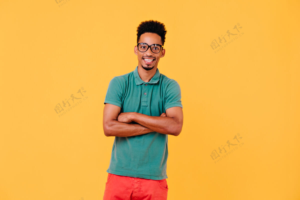 表情幸福的男模戴着眼镜站着感兴趣的短发黑人交叉双臂摆姿势现代活动微笑