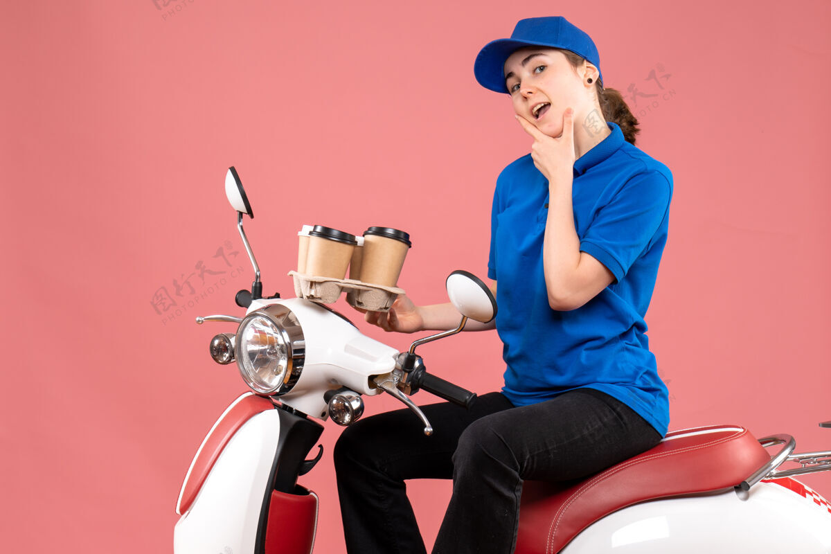 自行车正面图女快递员坐在自行车上拿着咖啡杯在粉色工作服上送工作人员食物坐着球员前面