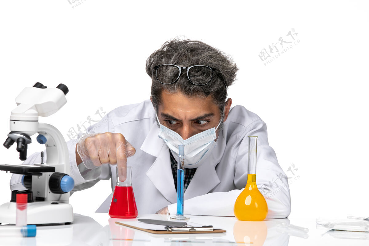 化学正面近距离观察穿着特殊套装的中年科学家坐在白色办公桌上拿着解决方案男性病毒科学冠状病毒-化学医生人员视图