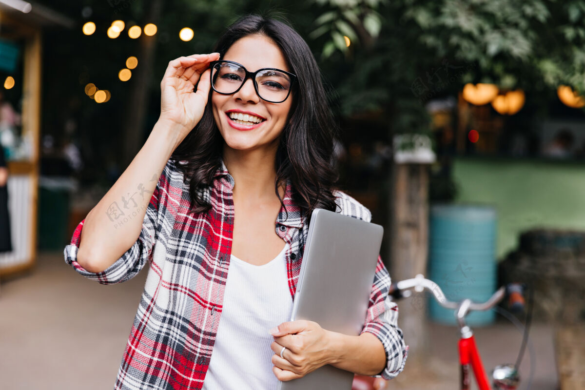 乐趣戴眼镜的女学生微笑着站在街上可爱的拉丁女人拿着笔记本电脑的画像大笑欧洲自由职业者