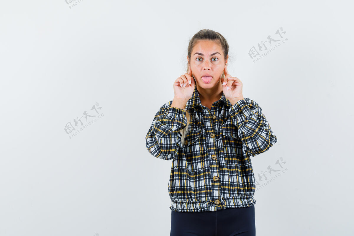 持有年轻的女士手指放在脸颊上 穿着衬衫 短裤伸出舌头 面带沉思棍子观点人