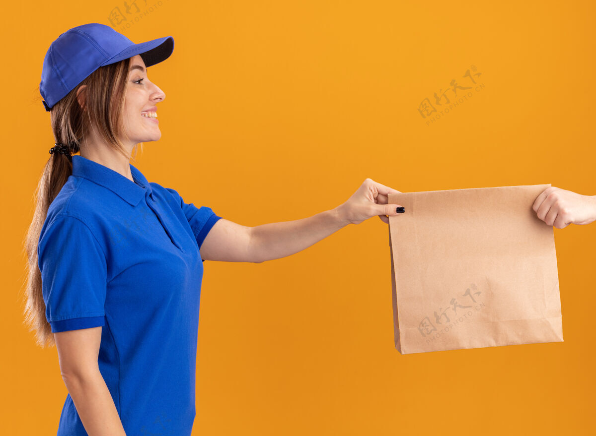 漂亮微笑着的年轻漂亮的女送货员 穿着制服 把纸包递给一个穿着橙色衣服的人制服摆姿势包装