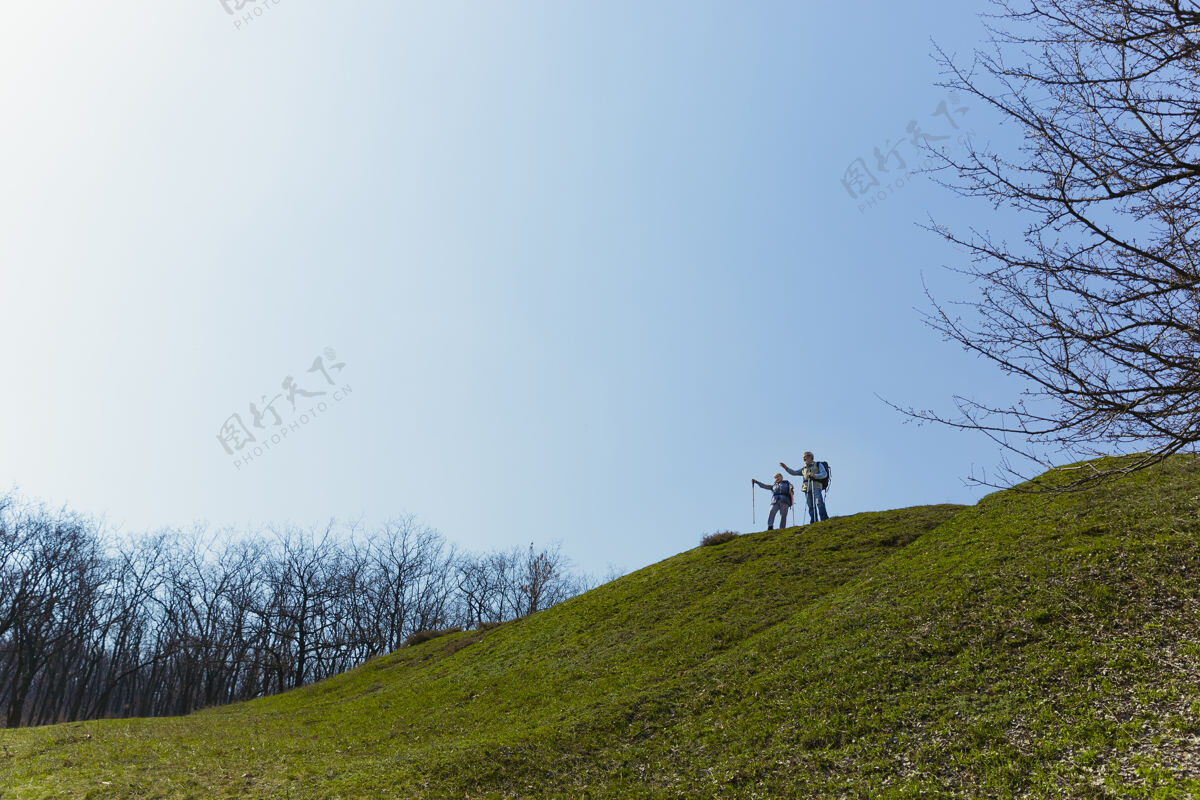 男性永远的自由阳光明媚的日子里 一对穿着旅游服装的老年夫妇在树旁的绿色草坪上散步旅游理念 健康的生活方式 放松和团聚周末一起成熟