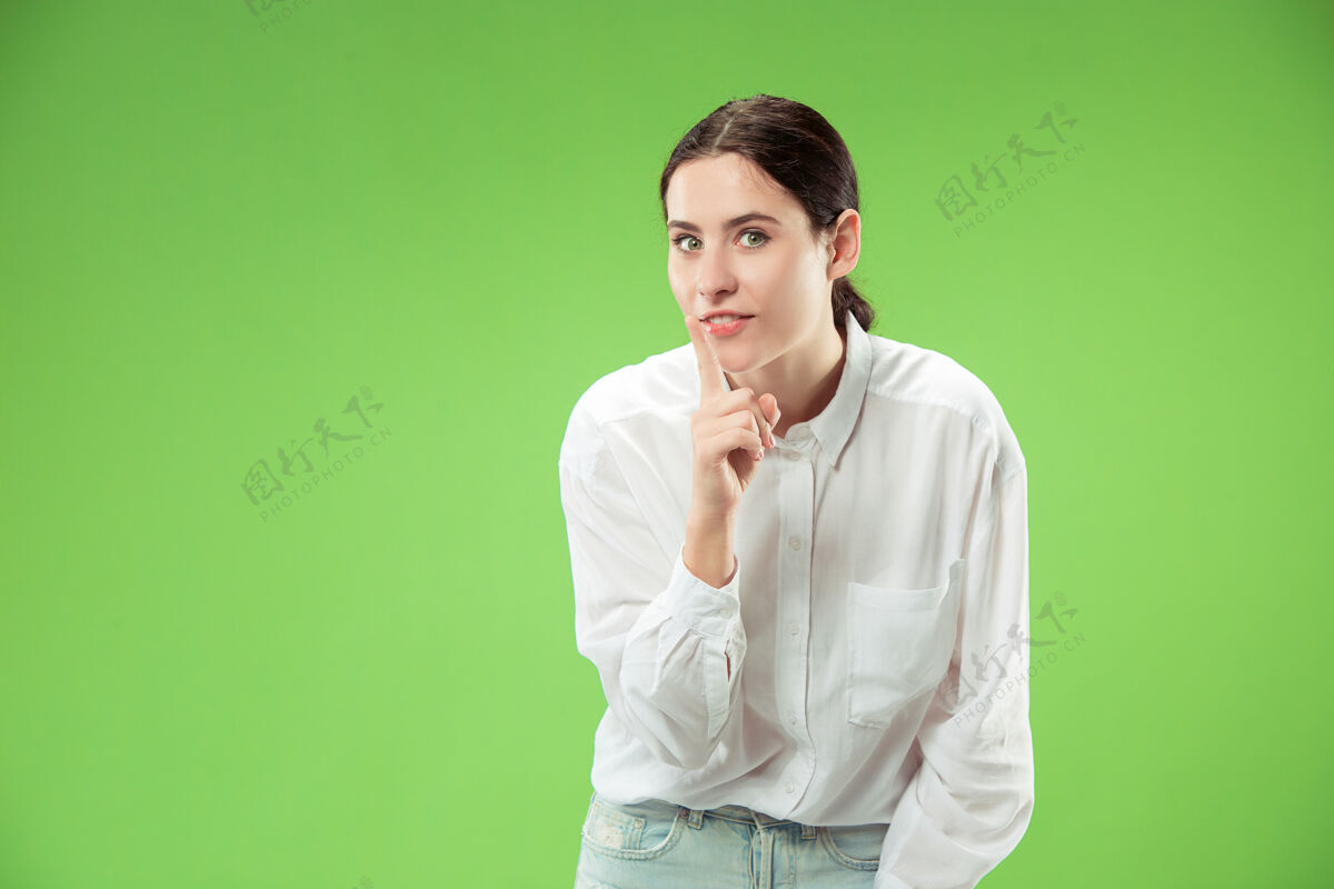 情感秘密 流言蜚语概念年轻女子在手后窃窃私语商业女性在时尚的绿色工作室背景下孤立年轻情感女性人类情感 面部表情概念乐趣朋友随意