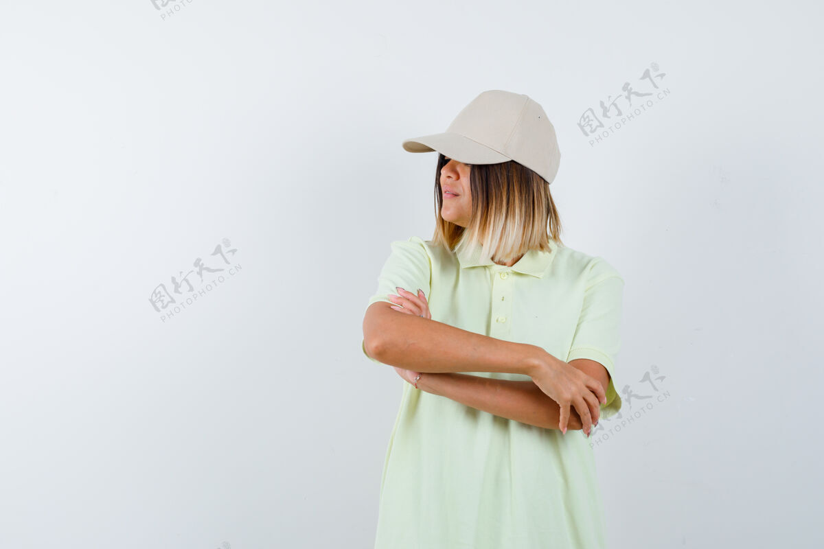 护理年轻女士交叉着双臂站着 一边看着远处的t恤衫 戴着帽子 看起来很自信 正前方的景色干净健康完美