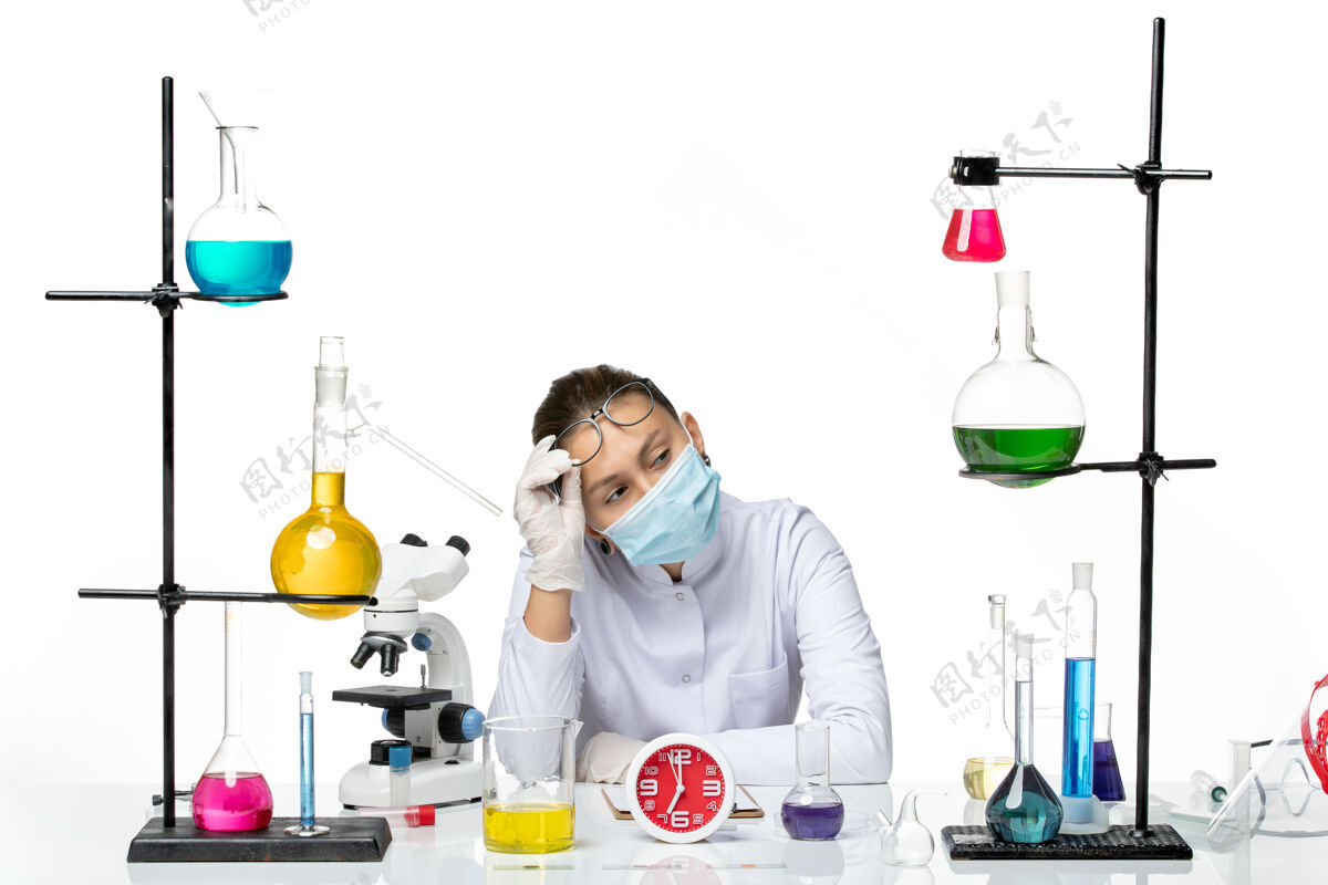 医学前视图穿着医疗服的女化学家 戴着面罩 坐在白色背景上 喷溅着病毒化学covid实验室的溶液医生实验室医学