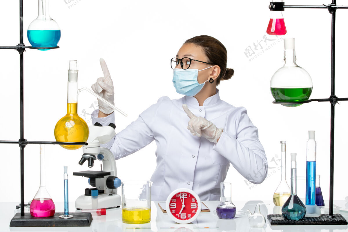 专业前视图穿着医疗服的女化学家带着面罩坐在白色背景上的溶液化学病毒-飞溅药物实验室病毒