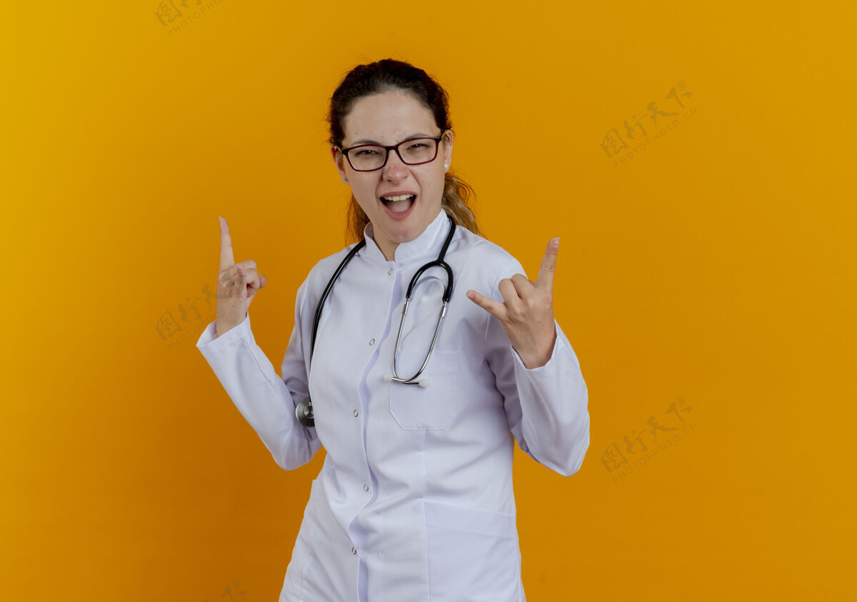 山羊年轻快乐的女医生 穿着医用长袍 戴着听诊器 眼镜上有山羊的手势眼镜女性女士