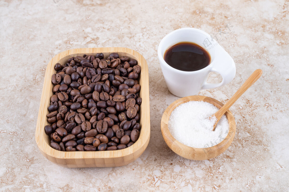 糖一堆咖啡豆放在木盘里 旁边是一小碗糖和一杯咖啡勺子咖啡因美味