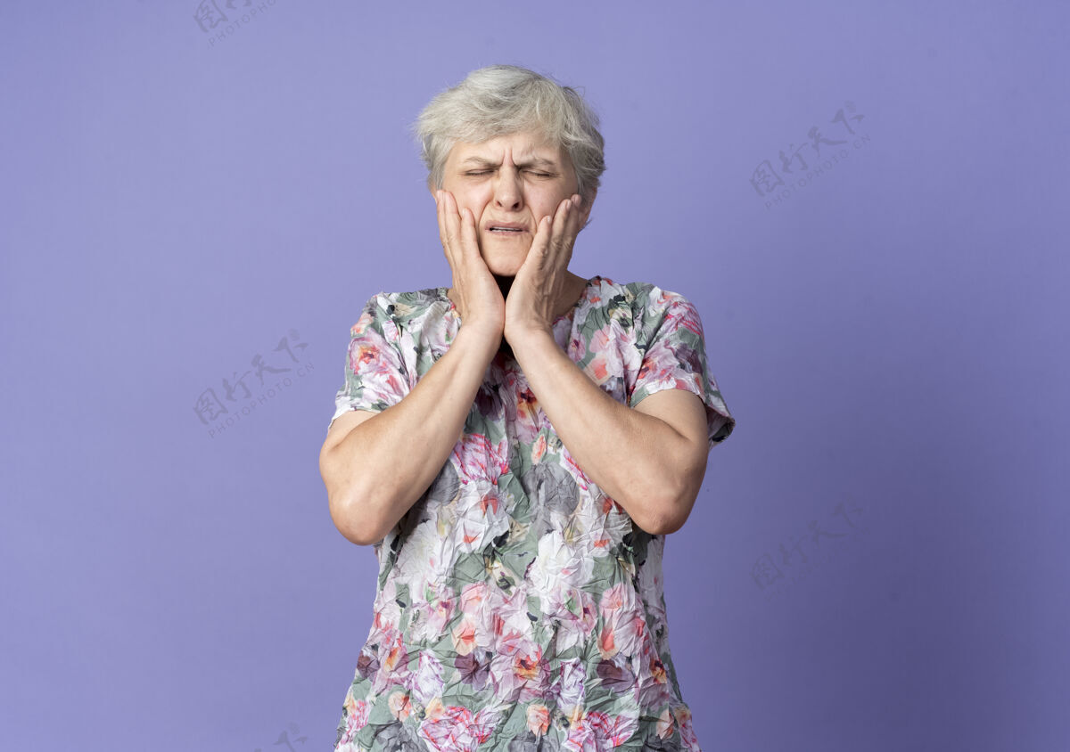 手疼痛的老妇人把手放在隔离在紫色墙上的脸上女人老紫