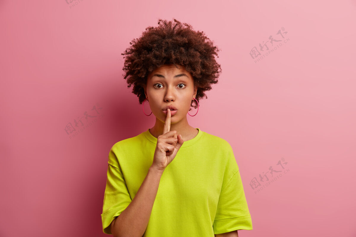 秘密请不要说话神秘的黑皮肤女人要求安静 把食指按在嘴唇上 要求安静 告诉秘密机密信息 隔离在粉红色的墙上 嘘休闲表达安静