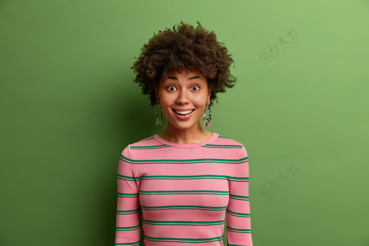 高兴喜笑颜开的非洲裔女子头像 神采奕奕 心情愉快 听到好消息 穿着休闲条纹套头衫 孤立在绿色的墙上情感概念表情年轻满意