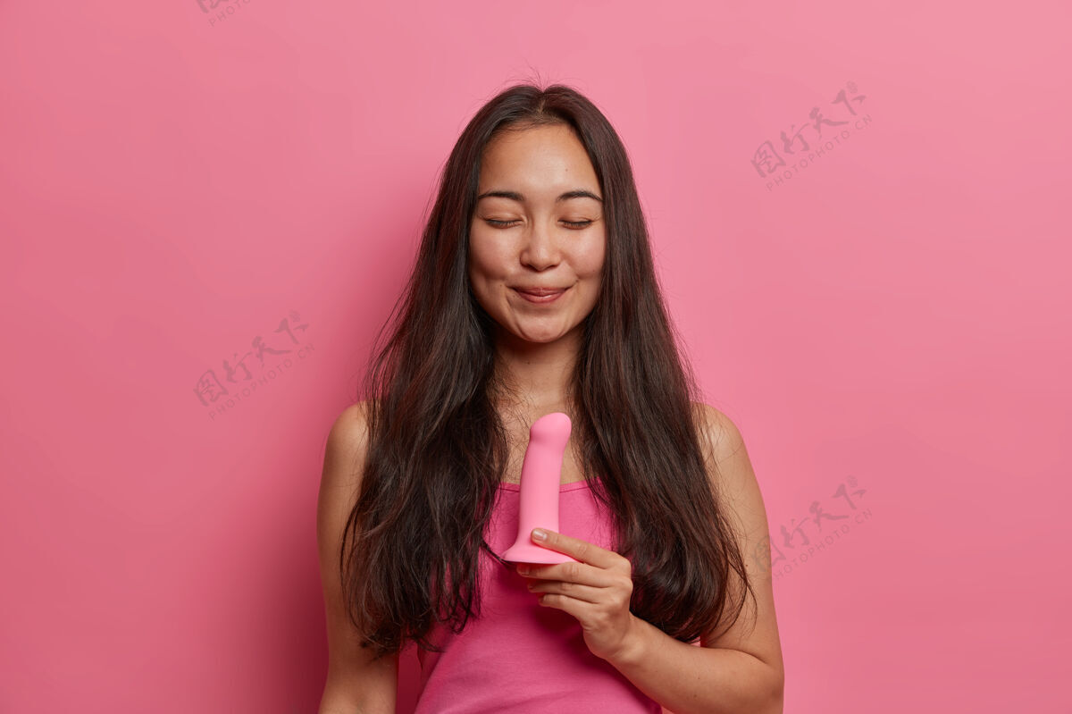 年轻喜笑颜开的黑发女人摆姿势 用硅胶假阴茎进行阴道 口腔或肛门的性渗透 不需要伴侣 刺激阴蒂 使用性玩具进行乳房按摩 站在室内刺激女人设备