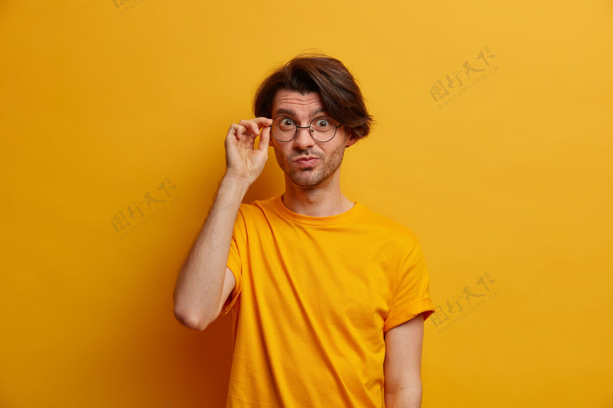 视图帅气好奇的男人透过眼镜聚精会神地看着 有着专注的目光 穿着休闲服 有着一丝不苟的神情 孤立在黄色的墙上 得到有趣的建议白种人表情注意