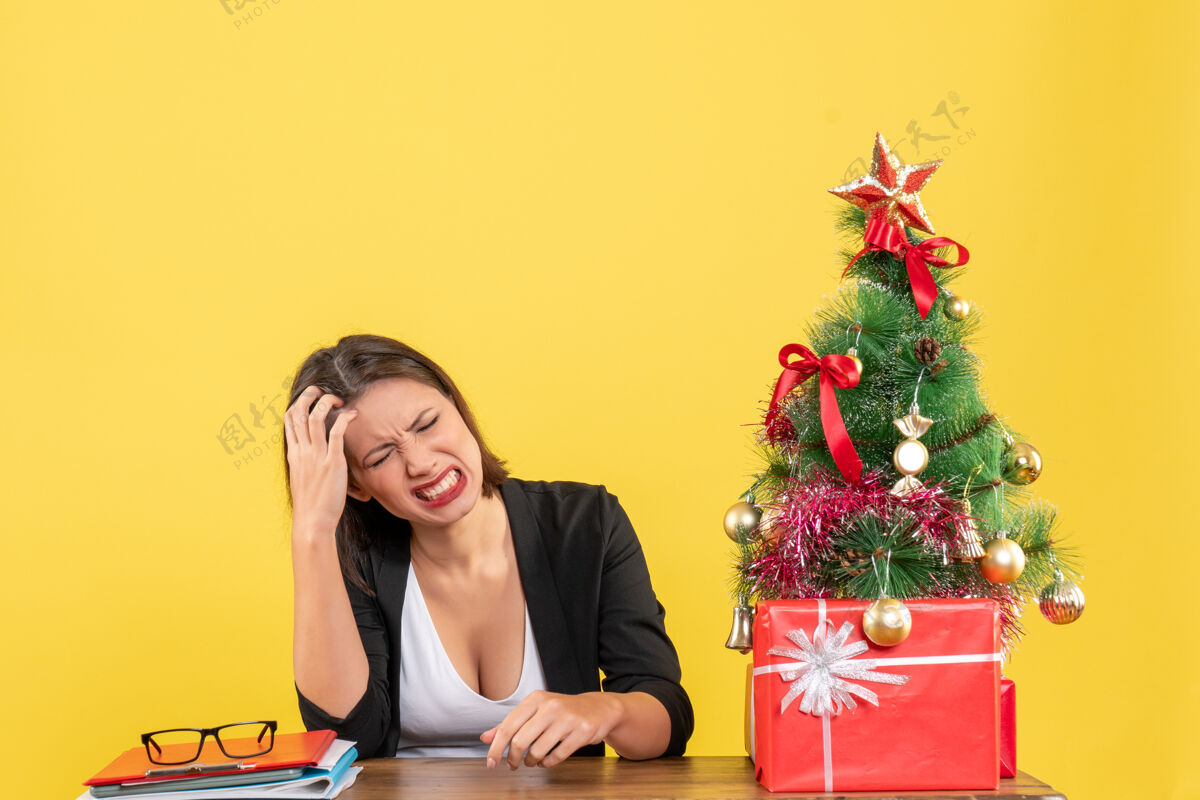 人在黄色的办公室里 一位年轻的女士穿着西装坐在一张桌子旁 旁边装饰着圣诞树成人桌子肖像