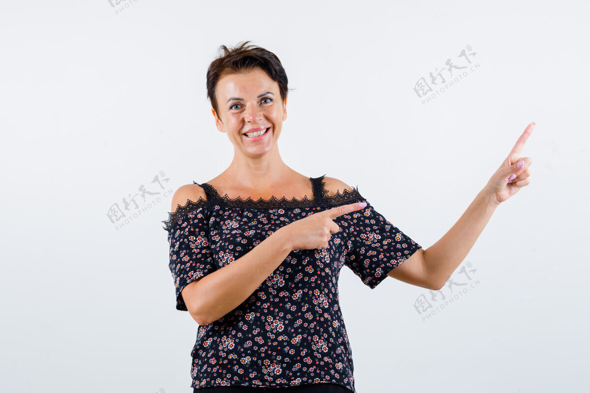 成人成熟的女人用食指指着右边的花衬衫 黑色的裙子 看起来很开心 正面视图花卉商务优雅