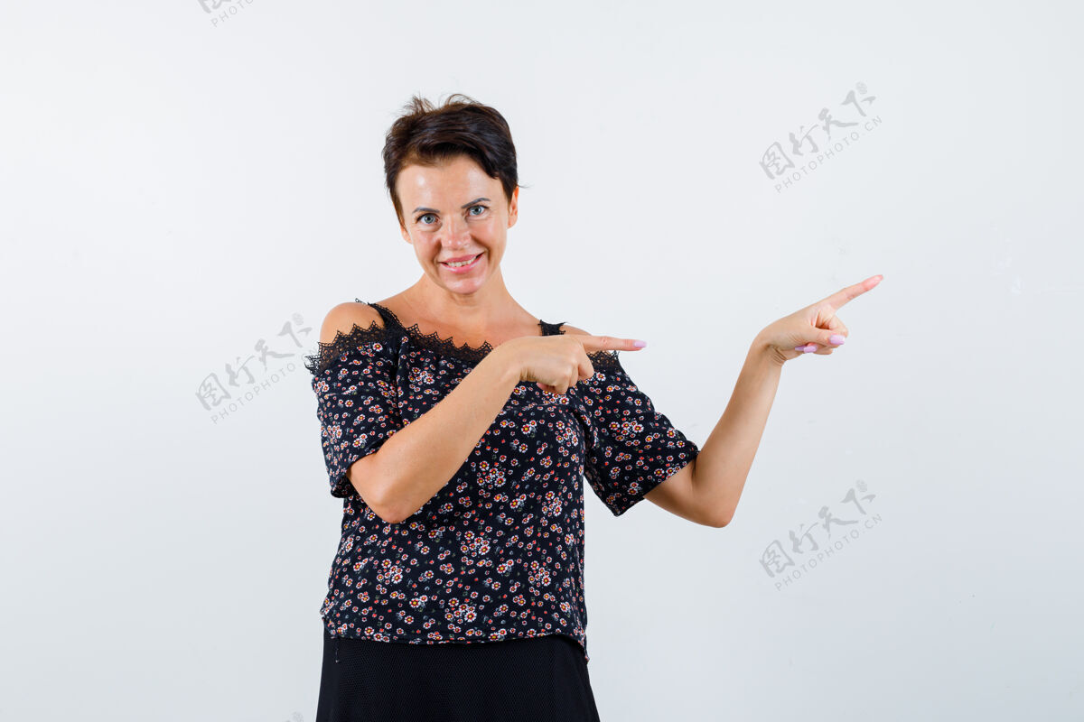人成熟的女人用食指指着右边 穿着花衬衫 黑色裙子 看起来很快乐 正面视图衬衫裙子正面