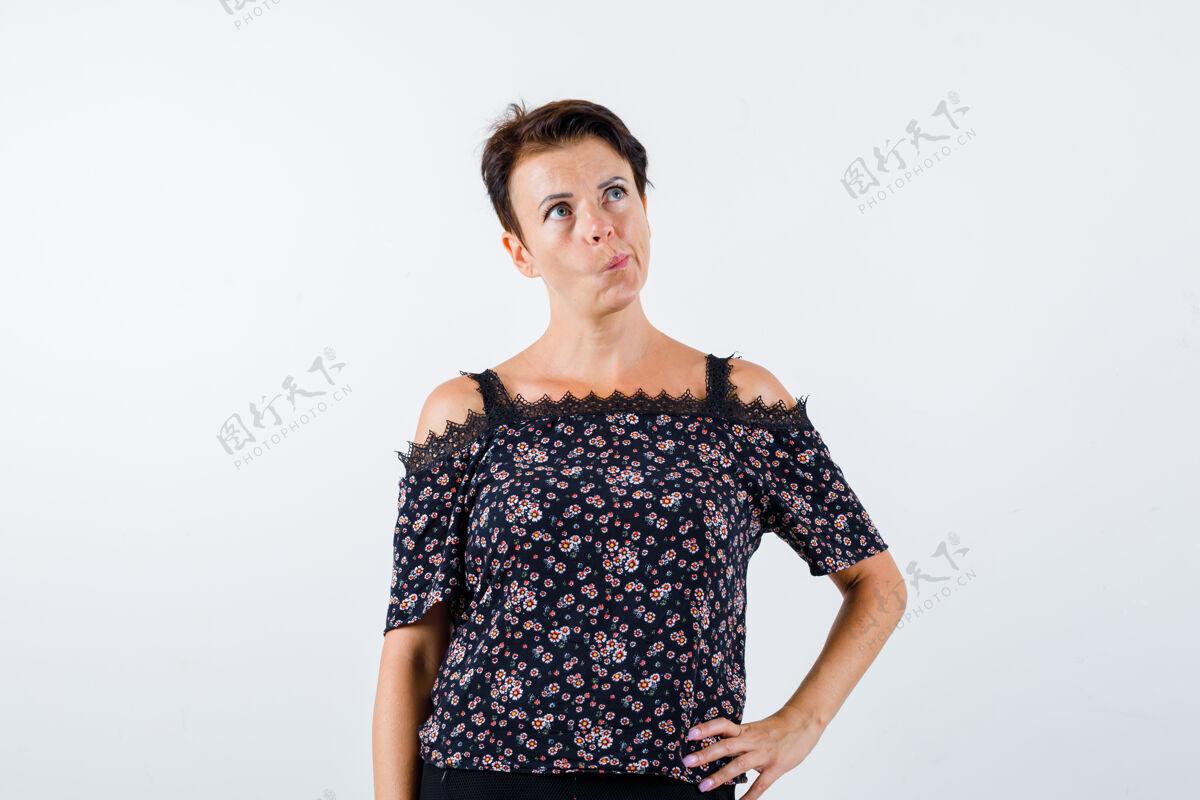 腰成熟的女人穿着花衬衫 黑色的裙子弯曲的嘴唇 手放在腰上 看起来沉思 前视持有人老年