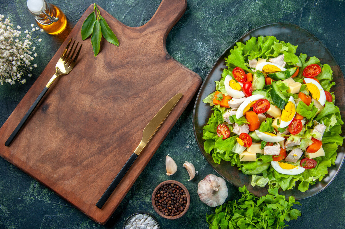 食物特写镜头下美味的沙拉与许多新鲜的原料香料油瓶大蒜餐具设置在木制砧板上瓶配料板