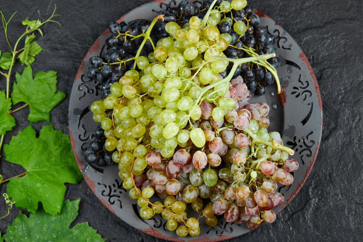 成熟在深色背景下 葡萄叶周围的一盘混合葡萄的顶视图高质量的照片串多汁季节