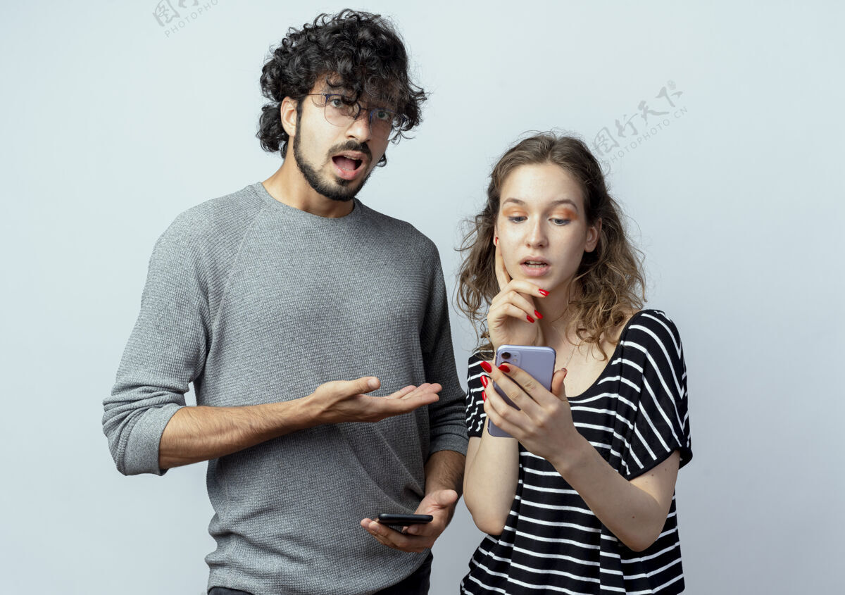 移动一对年轻男女 心烦意乱的男子指着拿着智能手机站在白色背景下的女友情侣心烦指着
