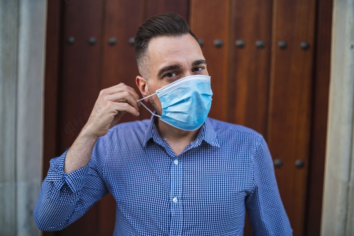 年轻人身穿蓝色衬衫 戴着医用面罩站在门口的年轻男性-covid-19概念医学男孩手