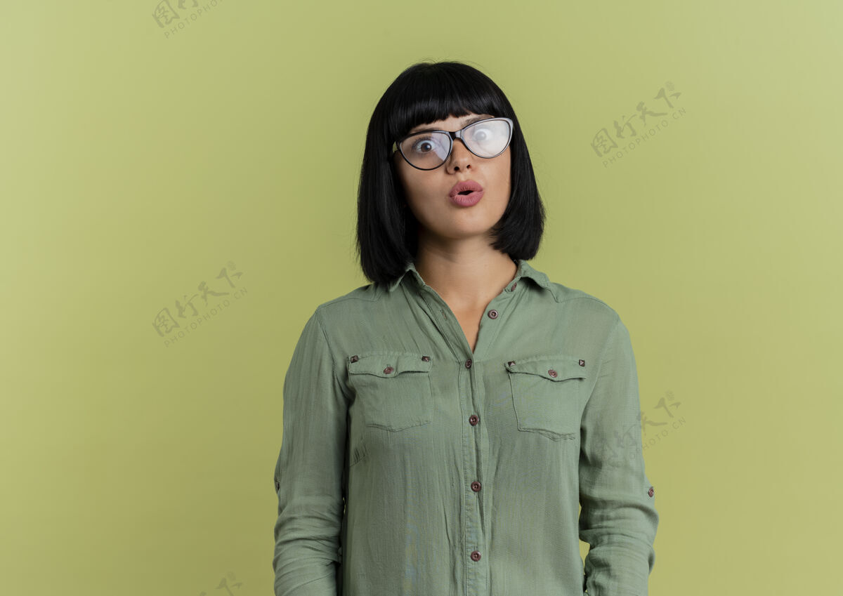 绿色震惊的年轻黑发白人女孩在光学眼镜看着相机孤立的橄榄绿背景与复制空间眼镜黑发复制