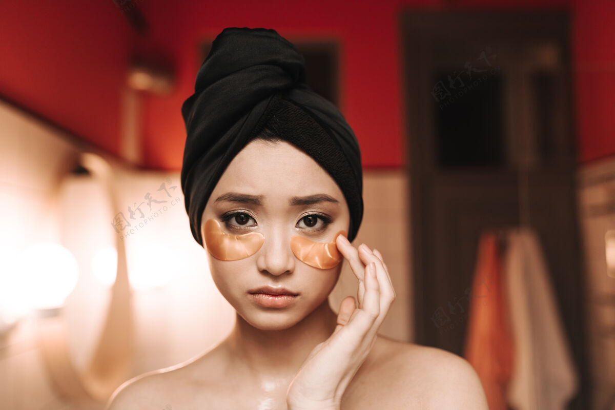 眼罩一幅悲伤的亚洲女人的肖像 戴着毛巾 眼睛下面有金色的补丁浴室脸头发