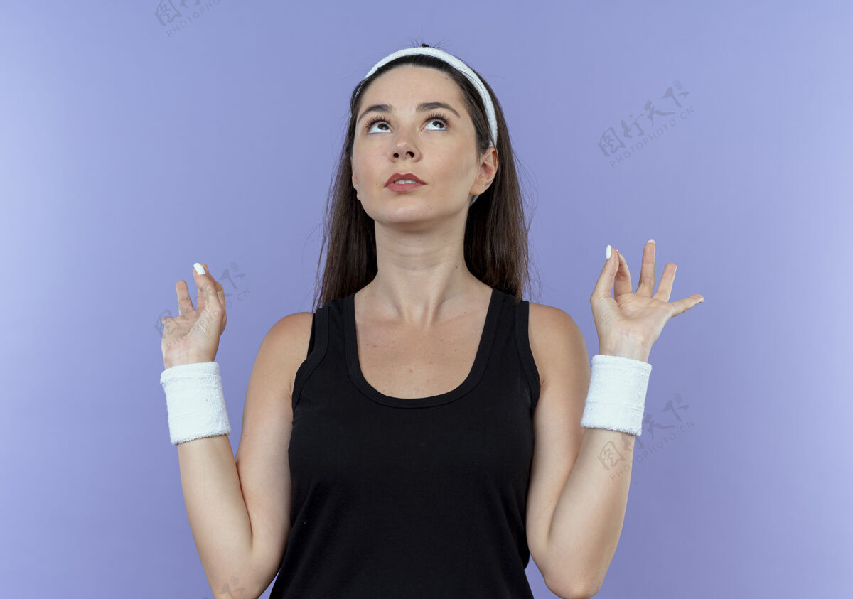 年轻戴着头巾的年轻健身女士抬起头做冥想手势 手指站在蓝色背景上头带手势健身