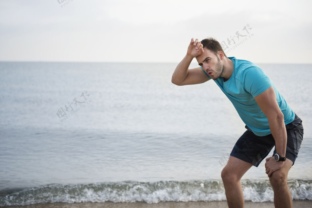 精疲力尽特写在海边慢跑的健康年轻人努力男人锻炼