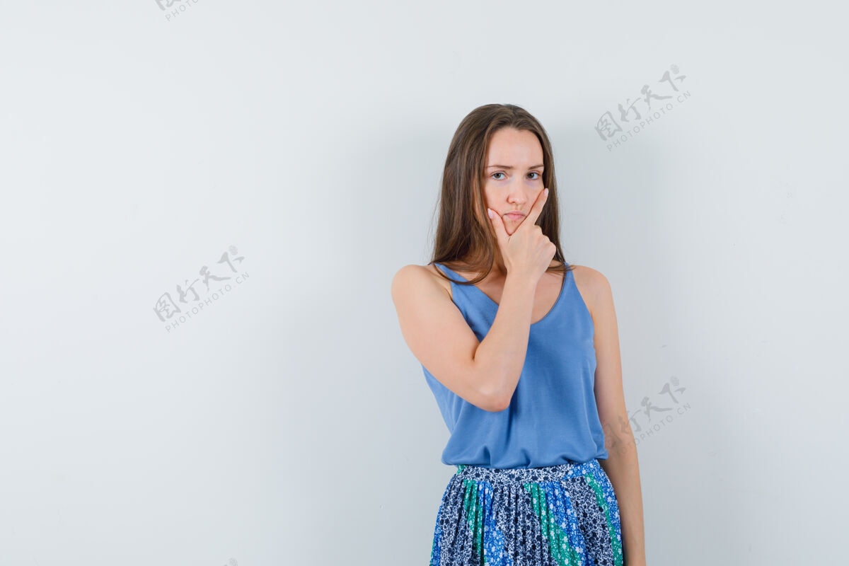 魅力年轻的女士手放在下巴上 一边想着蓝色的衬衫 裙子 一边若有所思地看着前面的景色空间放着文字豪华衬衫思考