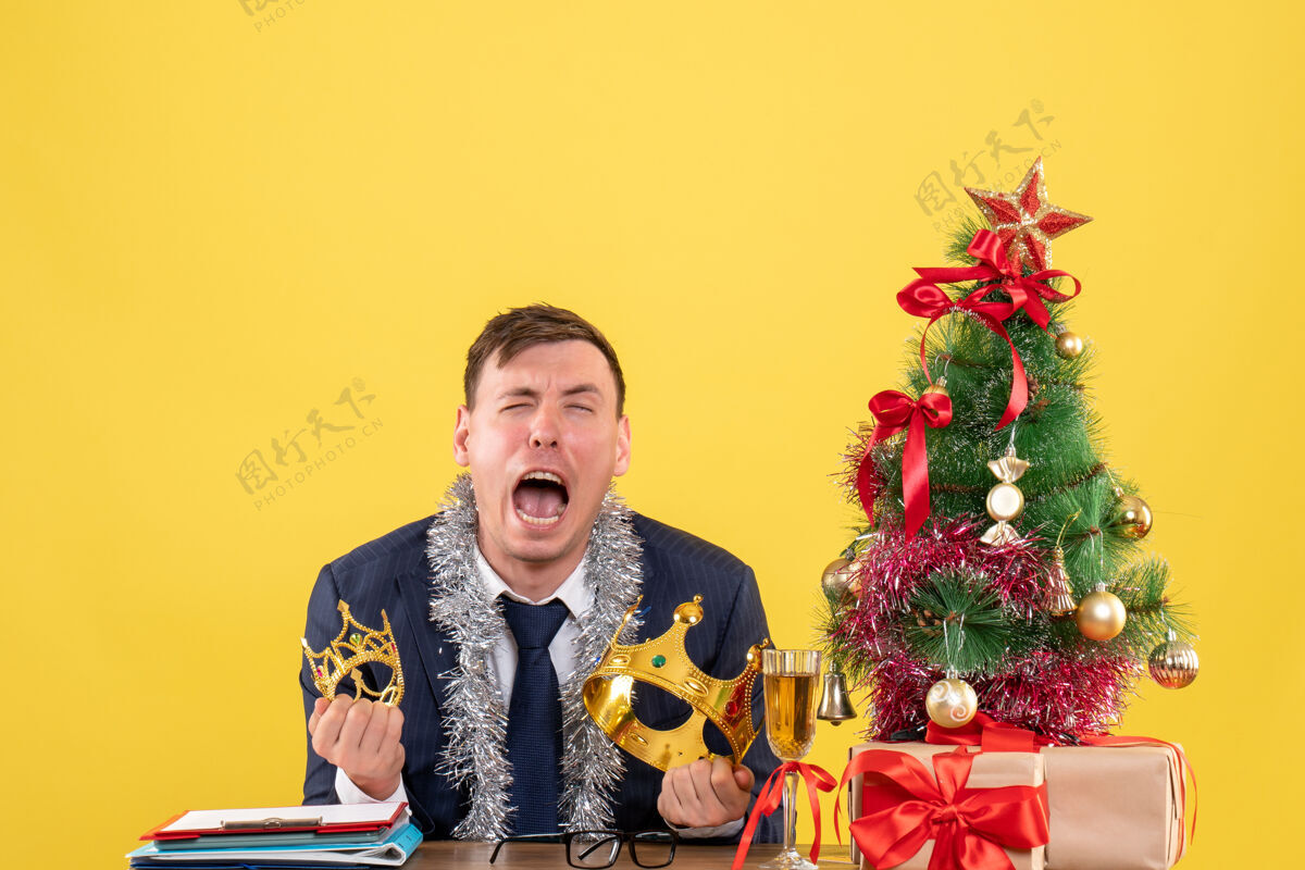 圣诞节前视图：商人坐在圣诞树旁哭泣 黄色背景下呈现生意男人前面
