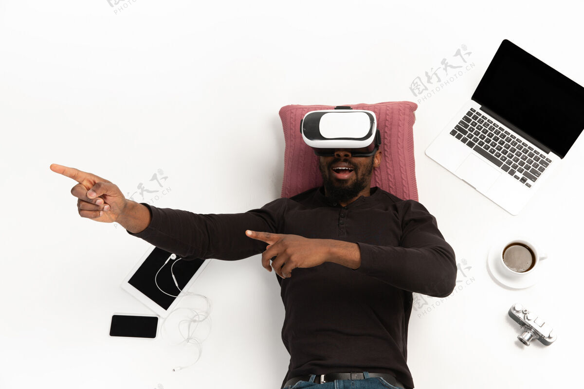 人情绪化的非裔美国人使用虚拟现实耳机周围的小玩意孤立的白色工作室背景 技术情绪化的发挥执行顶视图白色