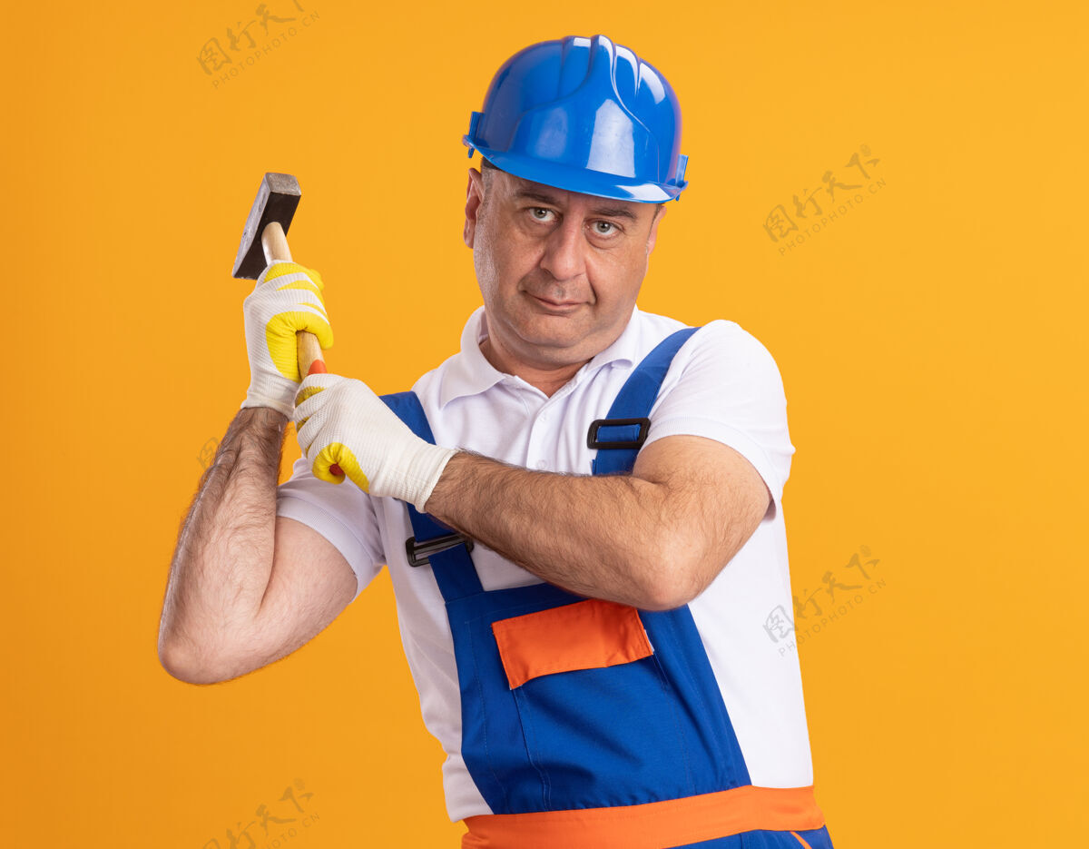公民高兴的成年建筑工人穿着制服戴着防护手套拿着锤子隔离在橙色的墙上衣服人姿势