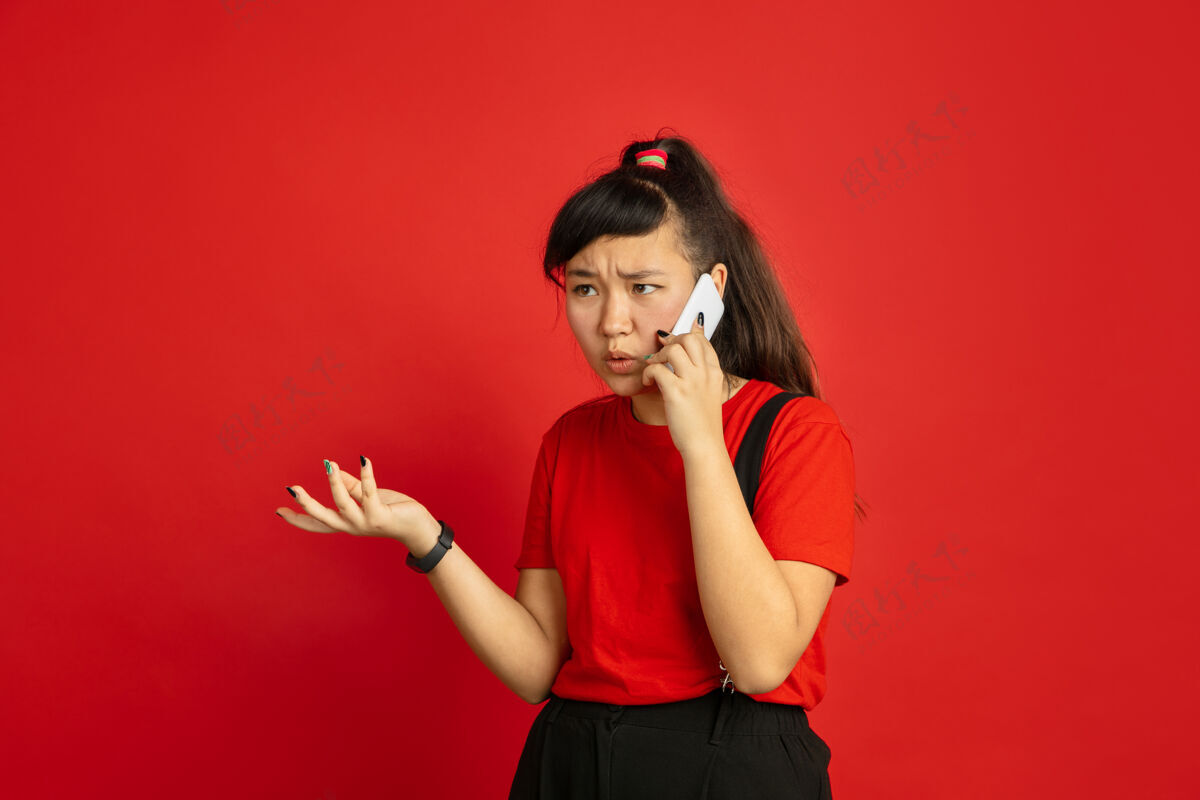 表情在红色工作室背景上孤立的亚洲青少年肖像美丽的深褐色女性模特 随意的长发人类情感的概念 面部表情 销售 广告电话交谈亚洲人年轻人手