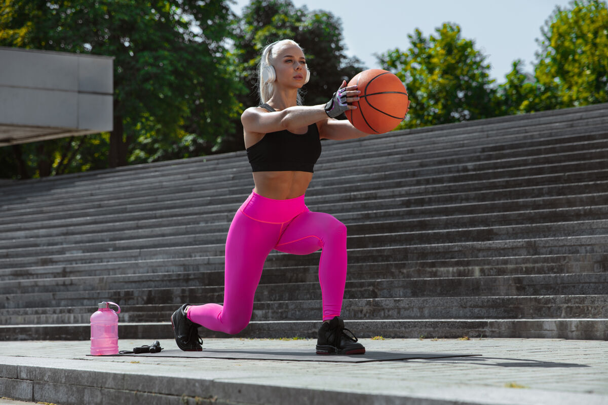 体育一个穿着衬衫 戴着白色耳机的年轻运动女性 在户外街头听音乐 带球做弓箭步 健康的生活方式 运动 活动 减肥的概念工作瘦减肥