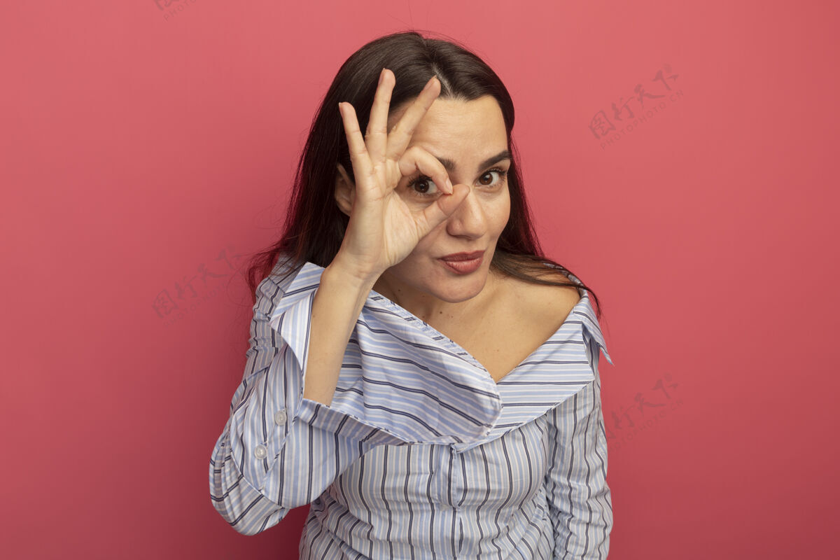 表情可爱的女人隔着粉红色的墙 用手指看着前面人通过感觉