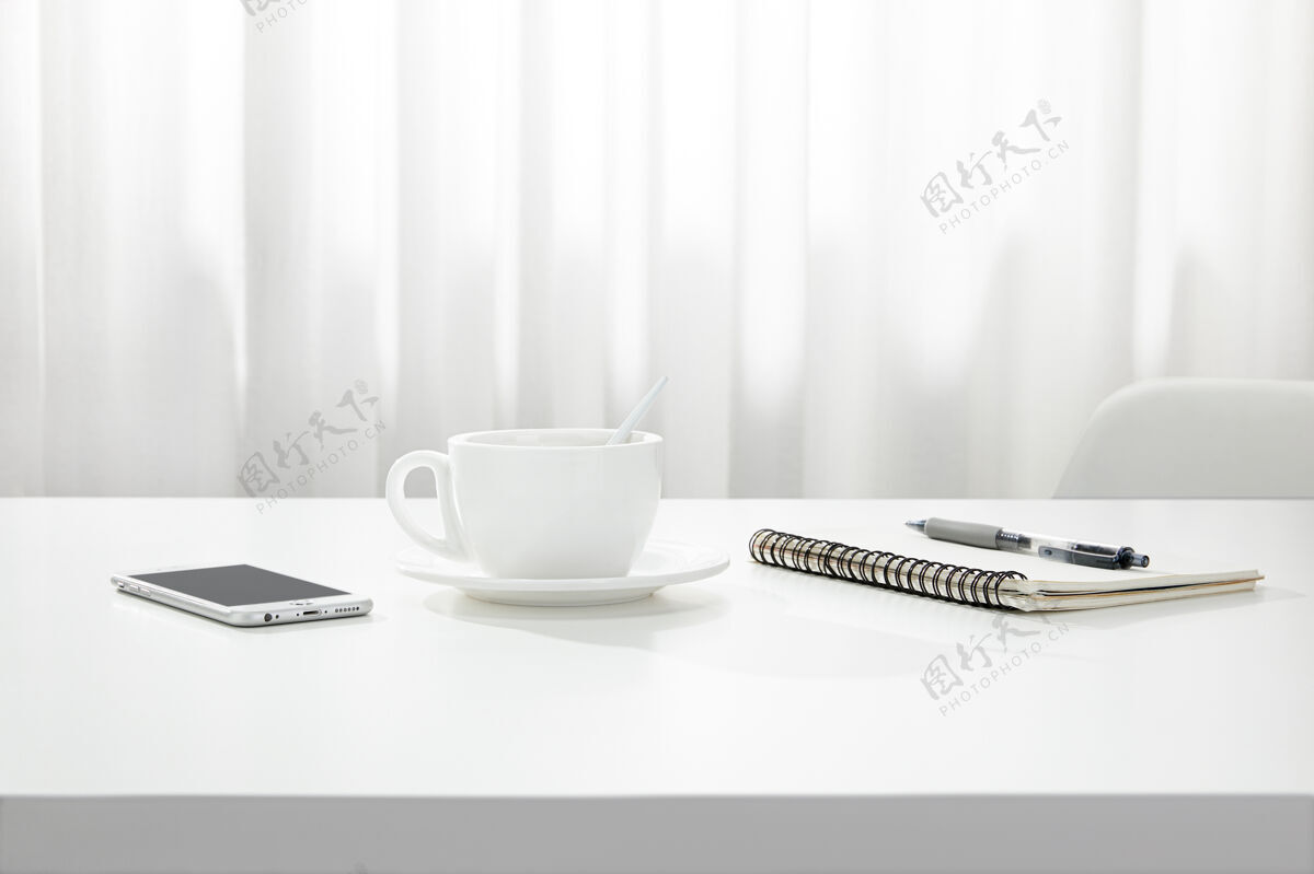 特写一杯咖啡 一本笔记本和一支笔 一部智能手机的特写镜头放在一张白色的书桌上 在室内纸张工作作业