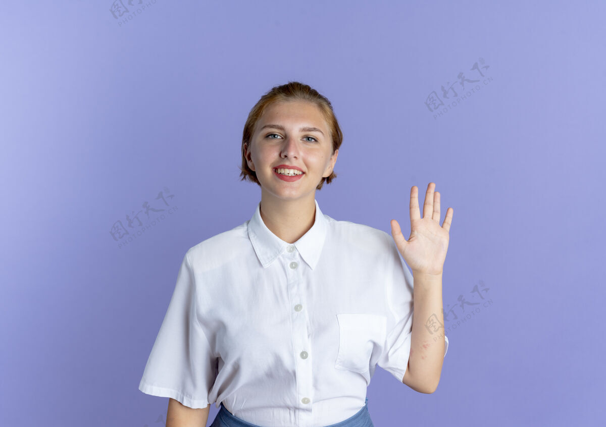俄罗斯年轻的微笑的金发俄罗斯女孩站着 举起的手孤立在紫色的背景与复制空间站起来女孩举起